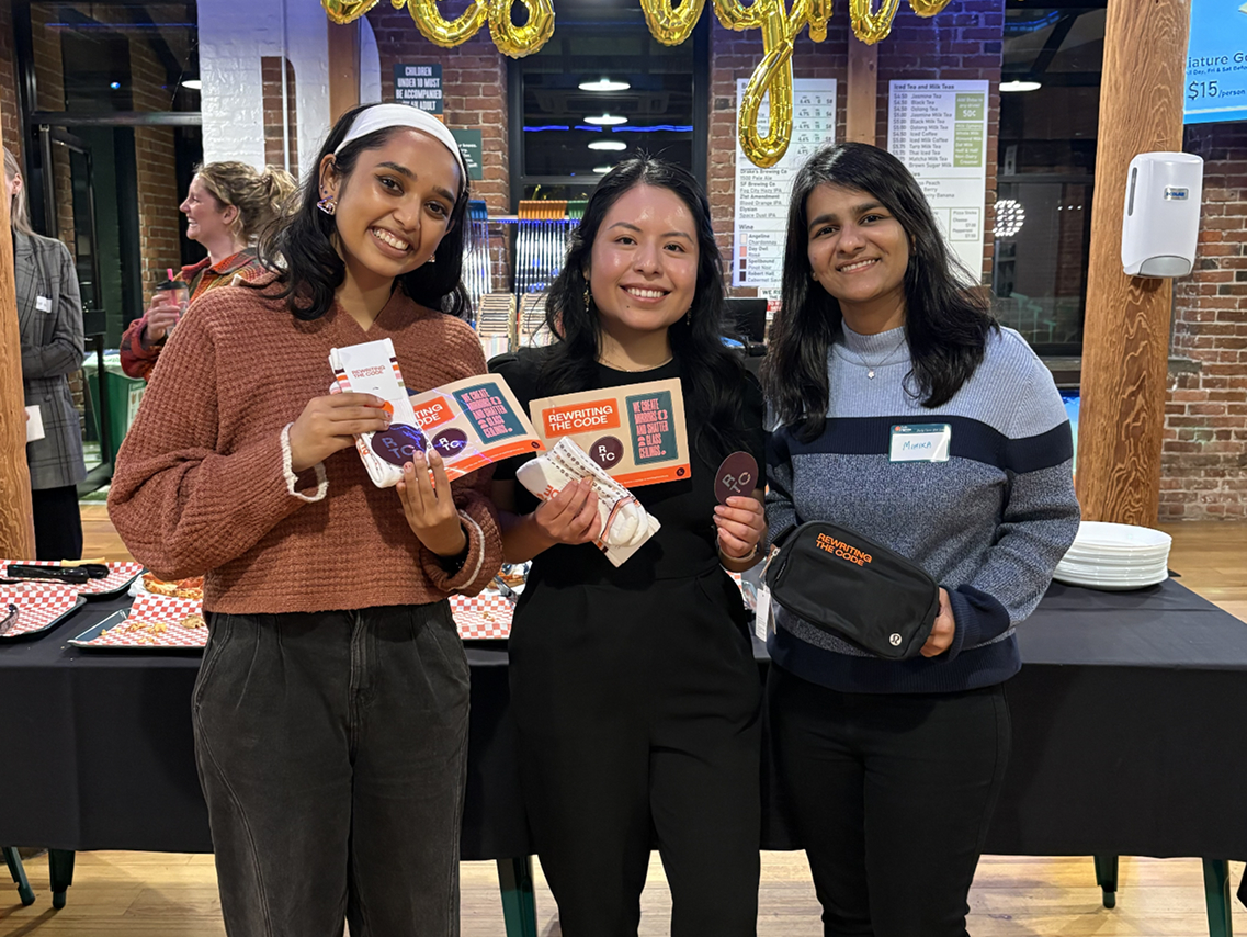 three women smiling and holding rewriting the code gear