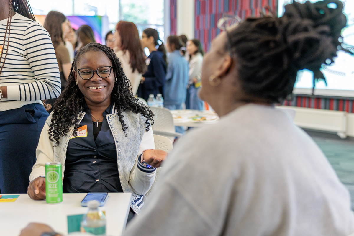 one woman in full focus smiling with another looking on